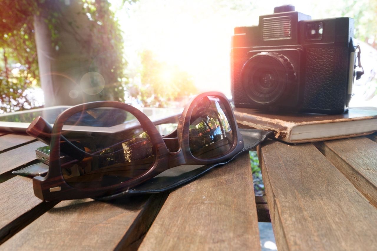Na imagem, um óculos e uma câmera fotográfica em cima da mesa.