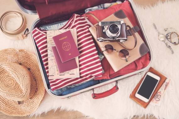 pacote de viagem Na foto, uma mala com roupas, documentos, acessórios e uma câmera fotográfica.
